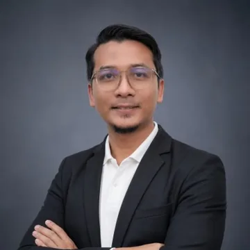 Aswadi Abdul Rahman, in glasses, a dark suit and an open-collared white shirt, smiling with his arms crossed against a gray backdrop.
